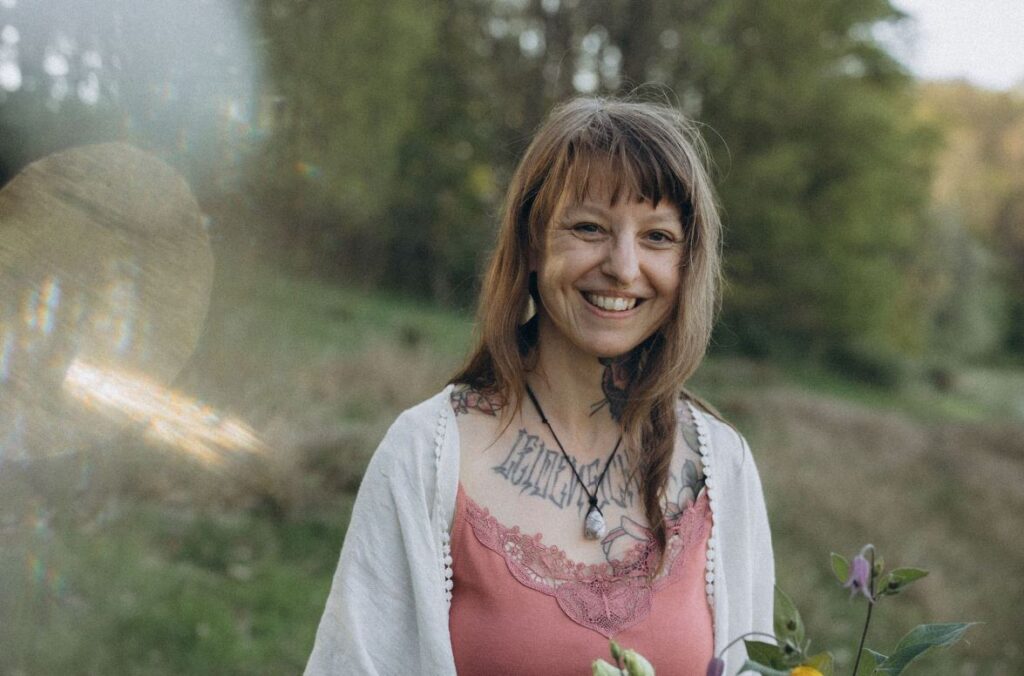 Angelina Katharina Petersen, steht lächelnd in der Natur, schaut direkt in die Kammera. Freut sich auf Begleitung in Leipzig