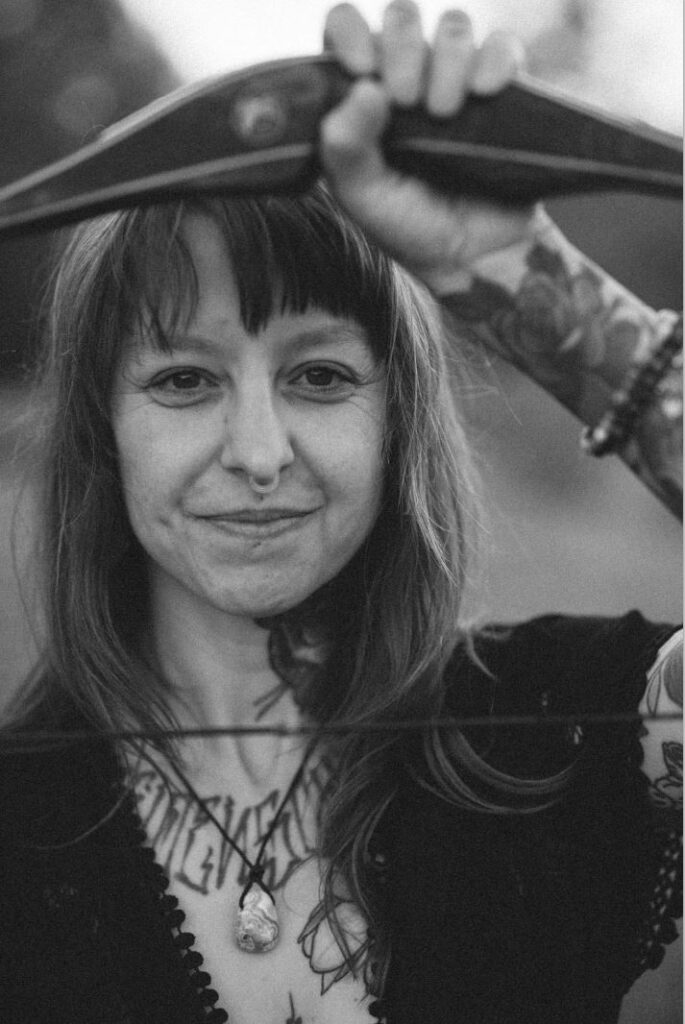 Angelina Katharina Petersen blickt direkt in die Kamera mit Bogen in der Hand – innere Stärke und Klarheit finden Leipzig