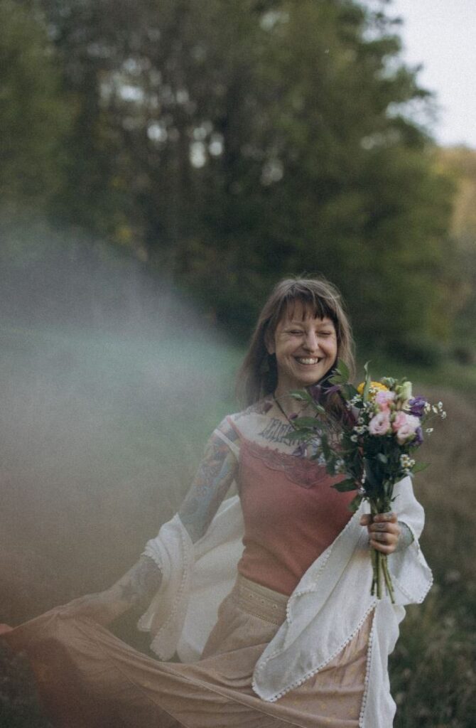 Angelina Katharina Petersen im weißen Kleid, lachend mit geschlossenen Augen, Blumenstrauß in der Hand, tanzend in der Natur