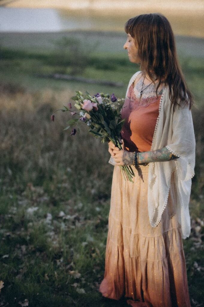 Angelina Katharina Petersen am See in Leipzig, mit geschlossenen Augen und Blumen in der Hand, Sonnenlicht im Gesicht, nach innen gekehrt