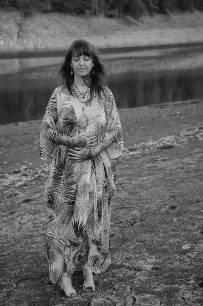 Angelina Katharina Petersen, steht in der Natur, die nackten Füße auf der Erde, Augen geschlossen, Hände auf dem Bauch. Sie spürt tiefe innere Ruhe