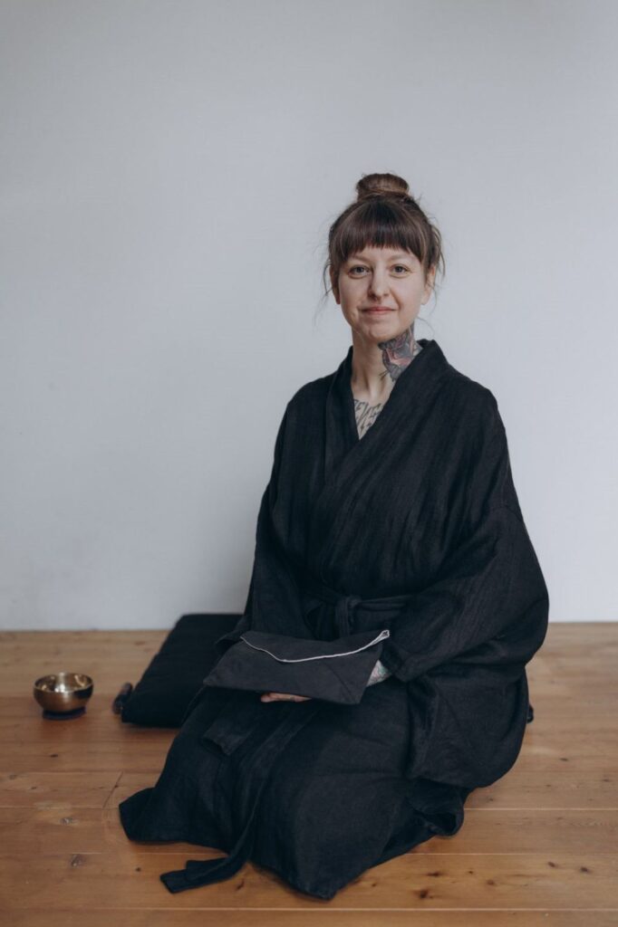 Angelina Katharina Petersen in schwarzem Zen Kimono, schaut in die Kamera. Die begleitet Menschen in Leipzig von Unruhe zu innerer Ruhe