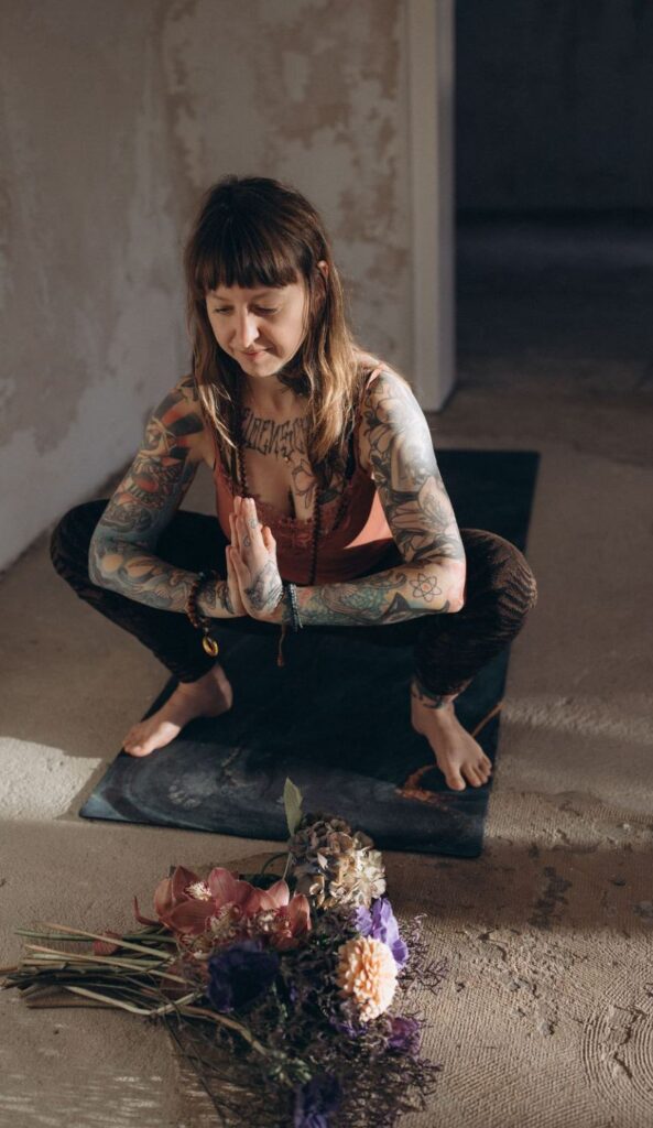 Angelina Katharina in sich gekehrt im Yoga Asana, mit Blumen und Händen in Namaste. Sie hilft Menschen aus der Angst in Leipzig
